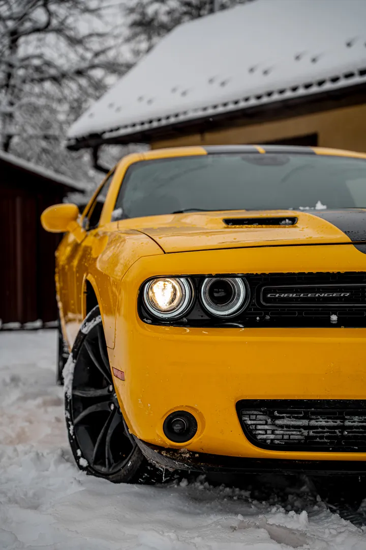 Żółty Dodge Challenger w śniegu, zapalony reflektor z bliska